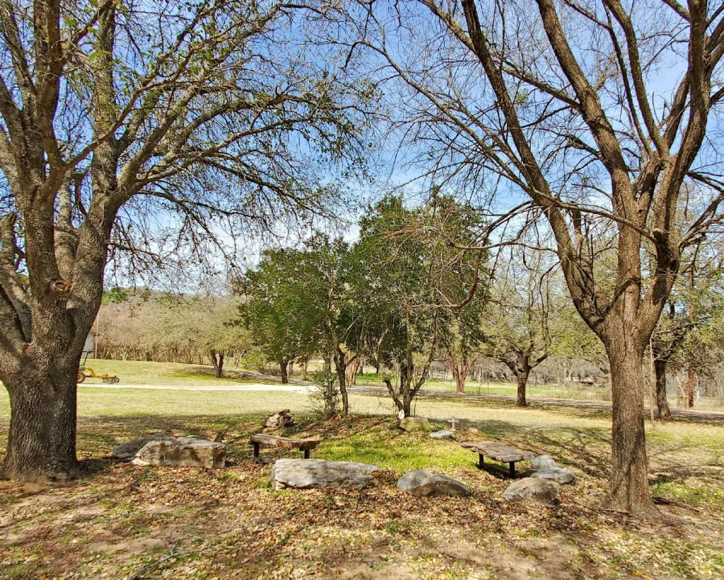 Quiet outdoor seating area with stone benches under large shade trees at Casa de Milagros, providing a peaceful environment for church staff to recover from burnout.